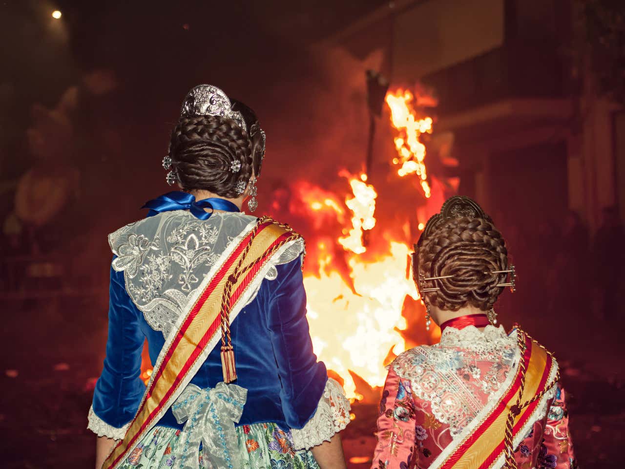 Dos falleras con sus trajes típicos contemplando el fuego de una falla