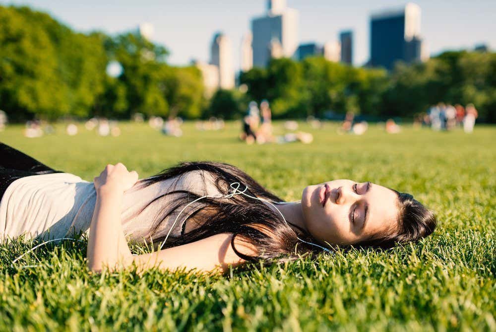 Femme allongée sur l'herbe avec des écouteurs dans les oreilles dans un parc