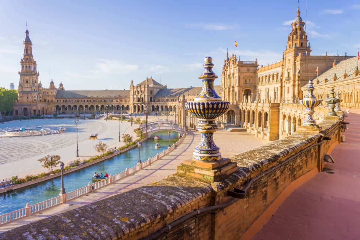 Scorcio del canale e degli edifici della Plaza de España di Siviglia in un giorno di sole, con muretto e vasi decorati in blu, giallo e bianco in primo piano