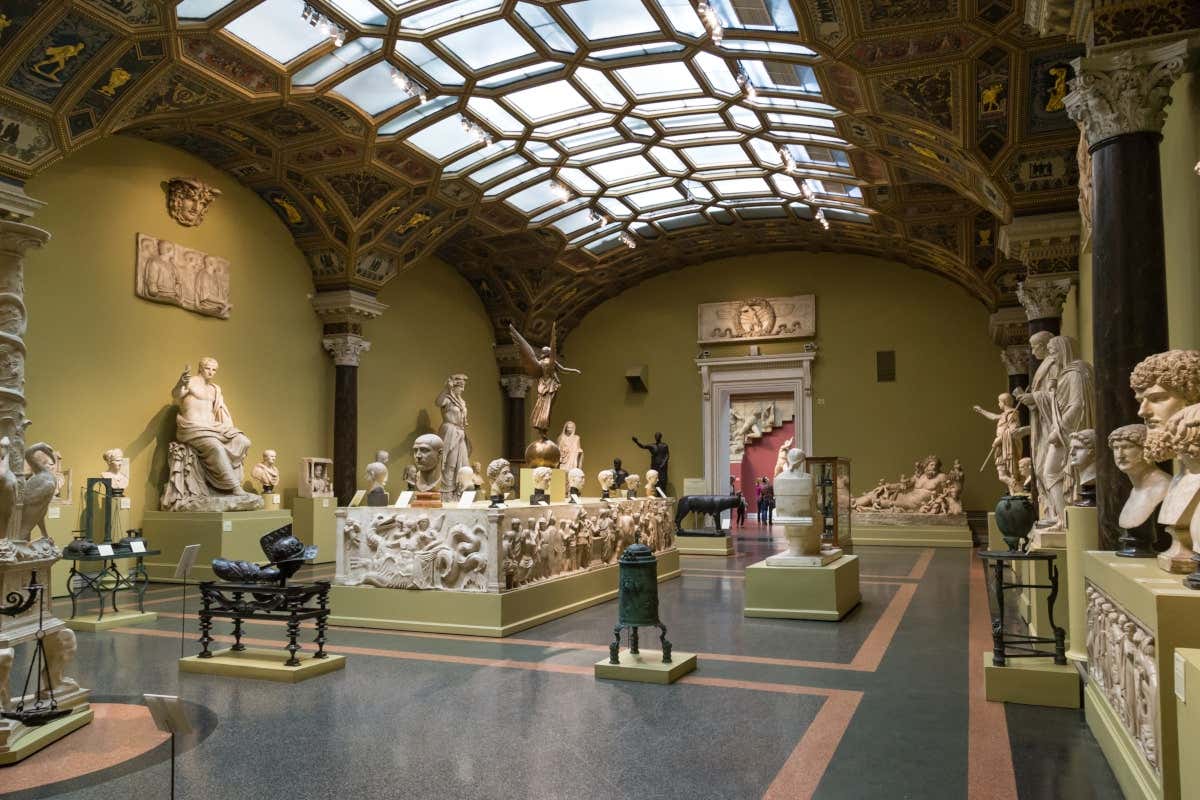 Una sala del Museo Pushkin con le pareti verdi e il soffitto di vetro, colma di statue di figure intere, busti, teste e altri oggetti