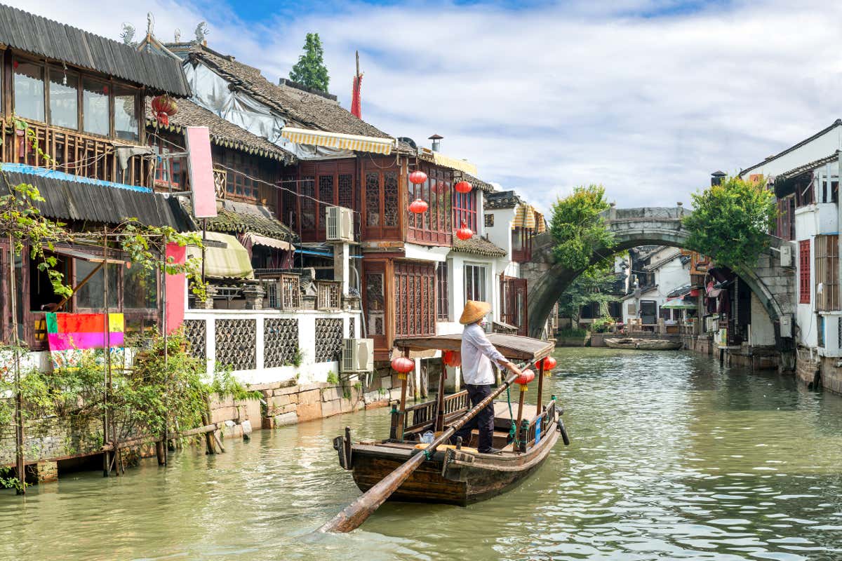 Barca tradicional china navegando por un río junto a las casas de una ciudad