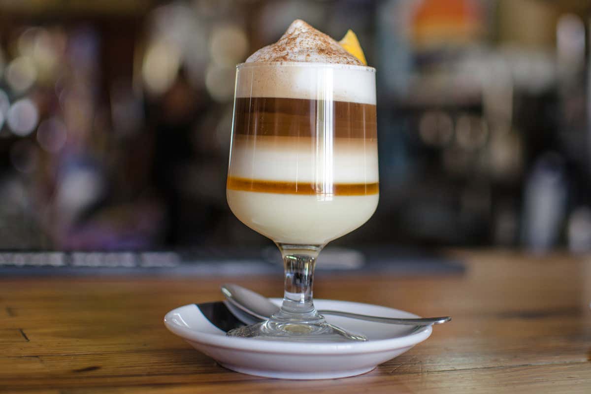 Une tasse en verre avec du lait concentré, du café, de la mousse de lait et du citron, le "barraquito" typique de l'île, à goûter lors de votre voyage à Tenerife