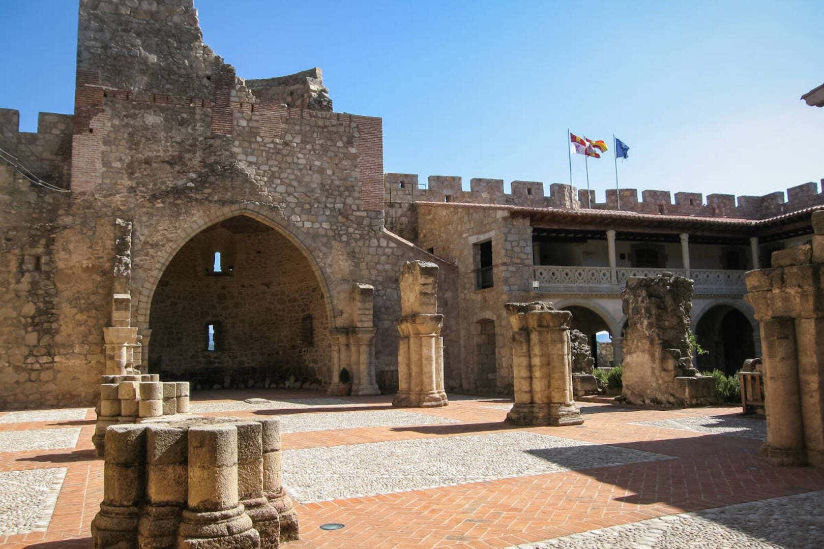 Ruinas de una iglesia con varias columnas de piedra y junto a un edificio con soportales