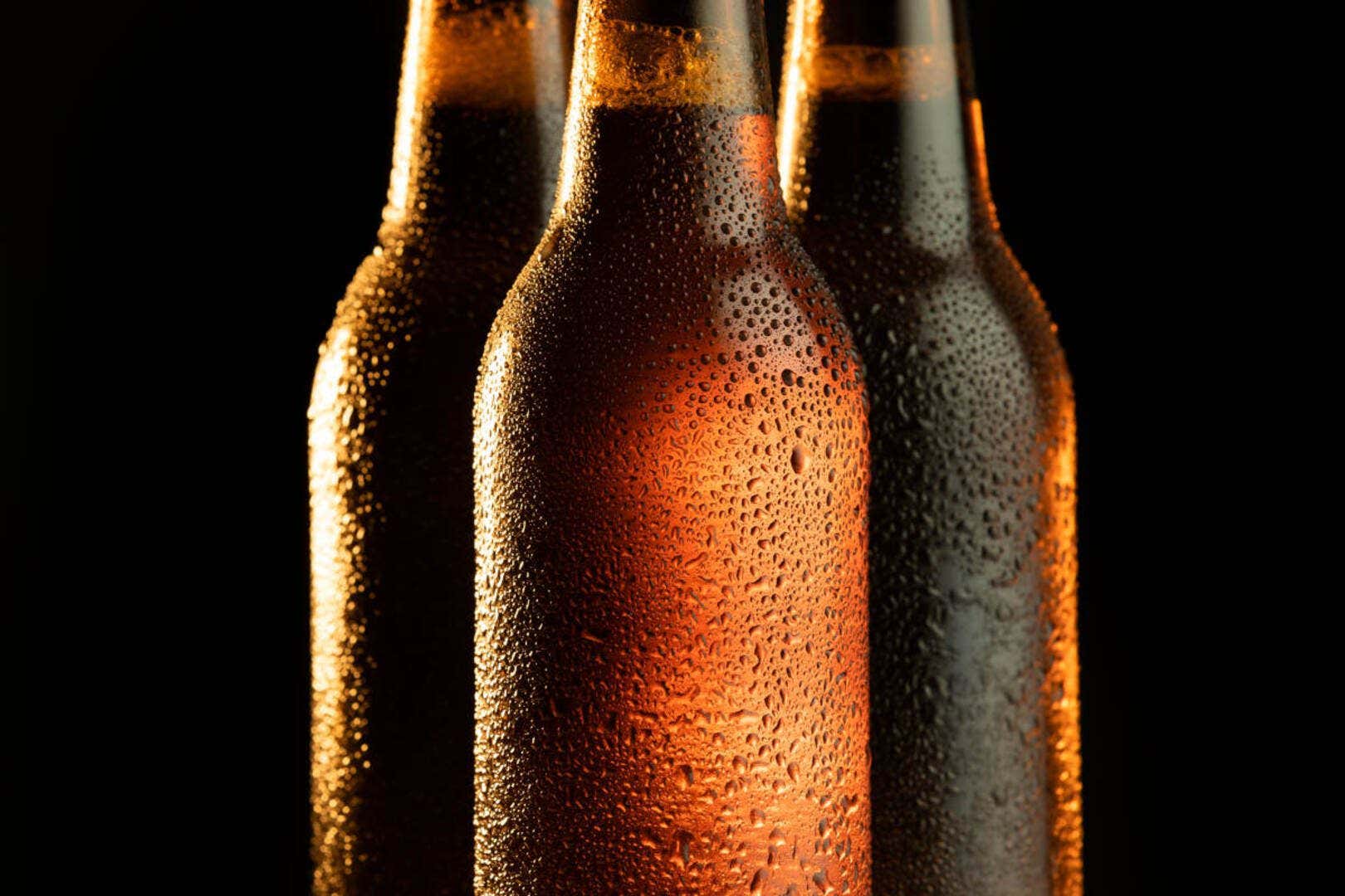 3 bottles of beer in brown bottles, with condensation on them and a black background.