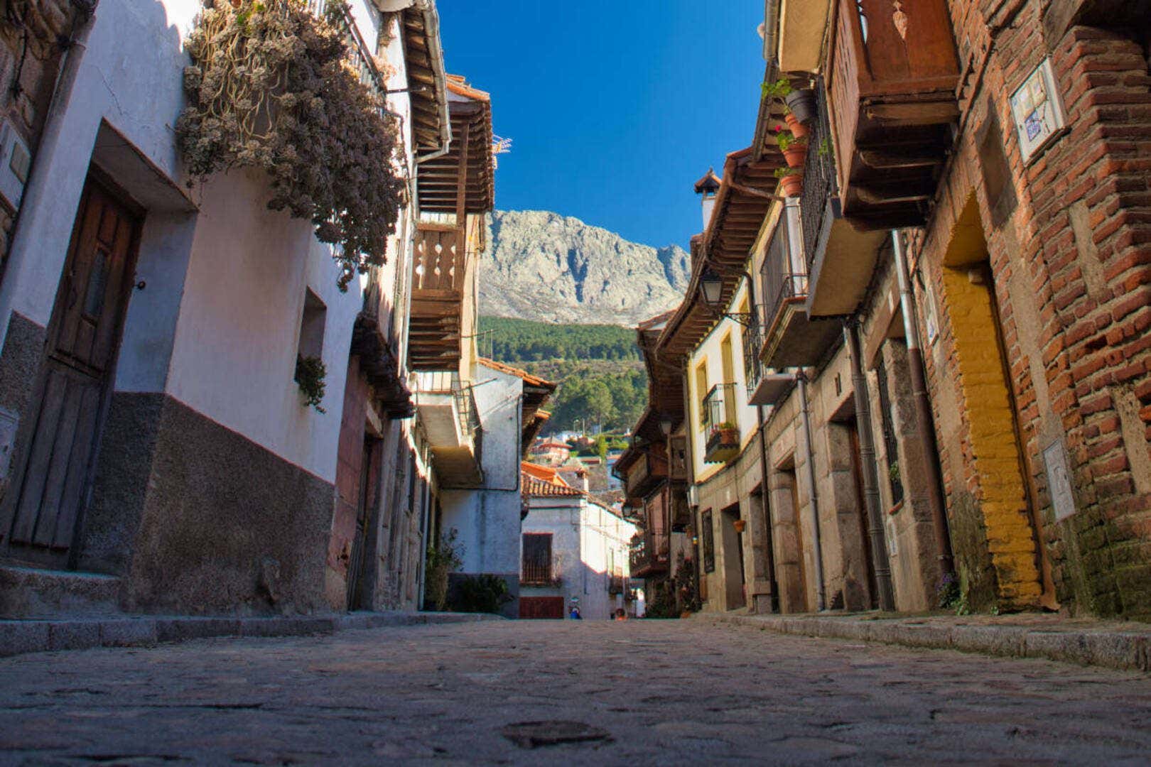 Una de las calles del casco antiguo de Cuevas del Valle con varias casas con balcones de madera y montañas al fondo