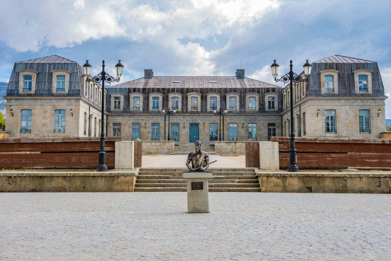 Fachada del palacio de los duques de Alba tras un busto de bronce en un día con algunas nubes