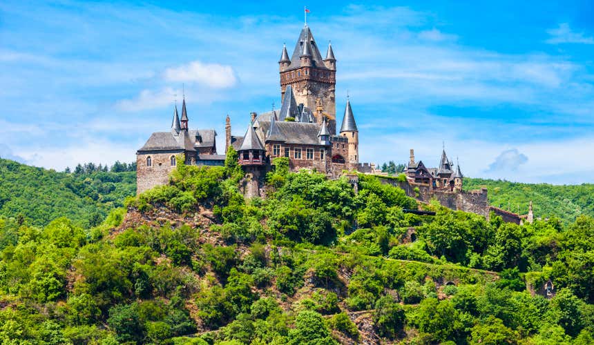 El castillo de Cochem con su gran torre central y sus tejados triangulares de color negro que destacan sobre la vegetación verde del entorno