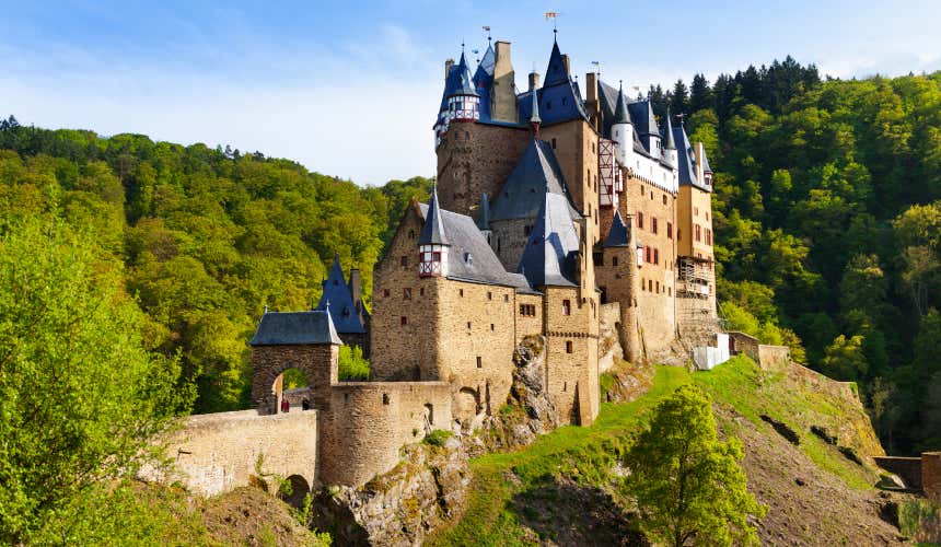 Panorámica del castillo de Eltz en lo alto de una colina rodeado por numerosos árboles de color verde intenso