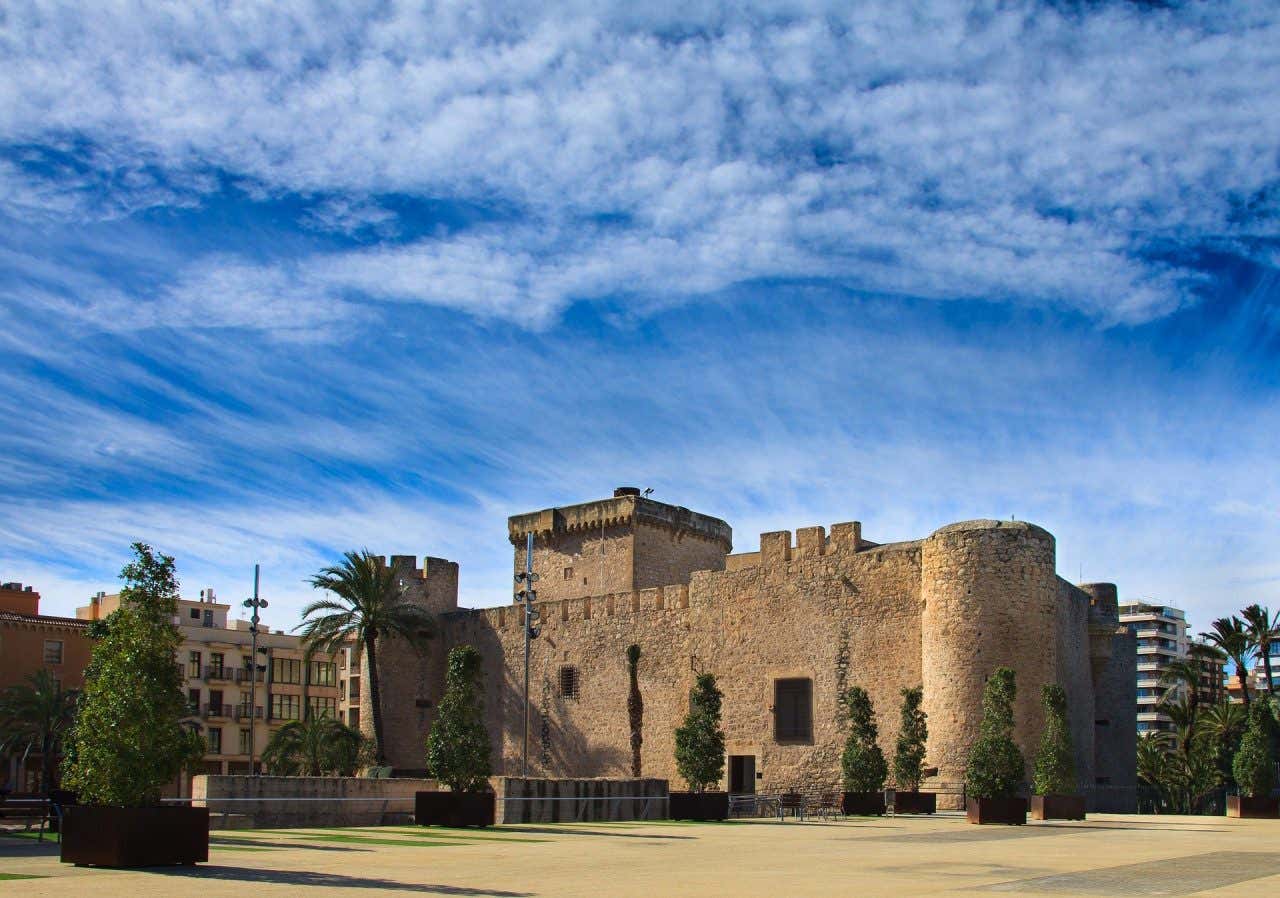 Palazzo di Altamira a Elce, circondato da palme e piante sotto un cielo nuvoloso.