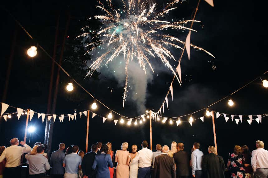 Invitados de una boda contemplan los fuegos artificiales que iluminan el cielo