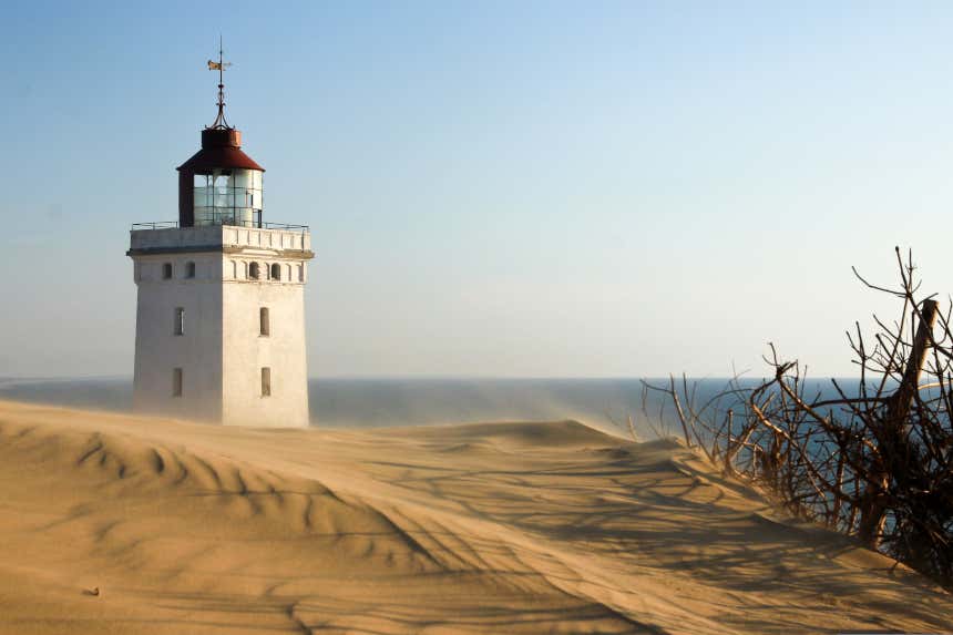 Un antiguo faro blanco asoma en un desierto junto al mar de la península de Jutlandia