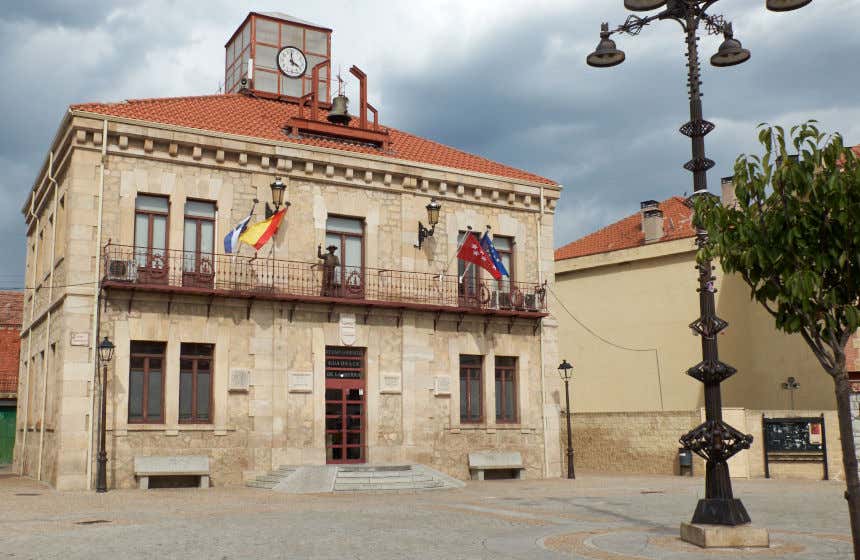 Fachada del Ayuntamiento de Gudalix de la Sierra, un edificio de piedra con dos plantas de altura y una pequeña campana y reloj en el tejado.