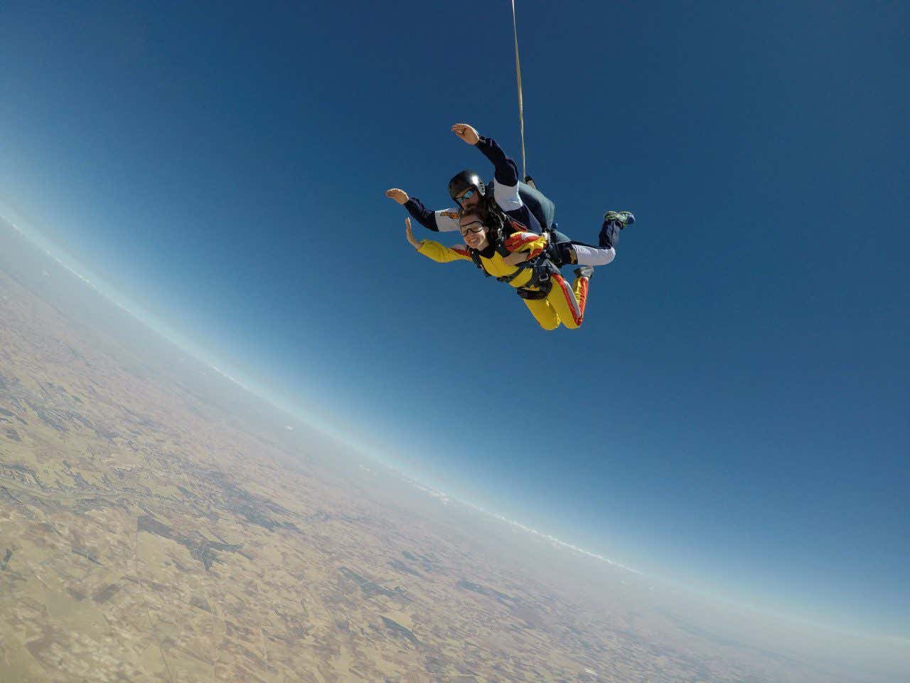 Anna Bondareva en el cielo azul acompañada por un instructor mientras se lanza al vacío en una actividad de salto en paracaídas.