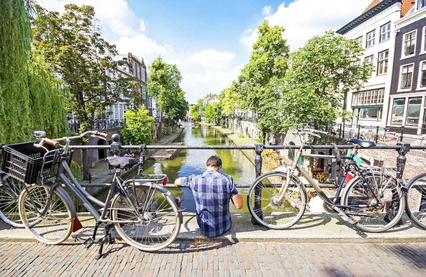 Un jeune homme assis sur un pont à Utrecht à côté de deux vélos.