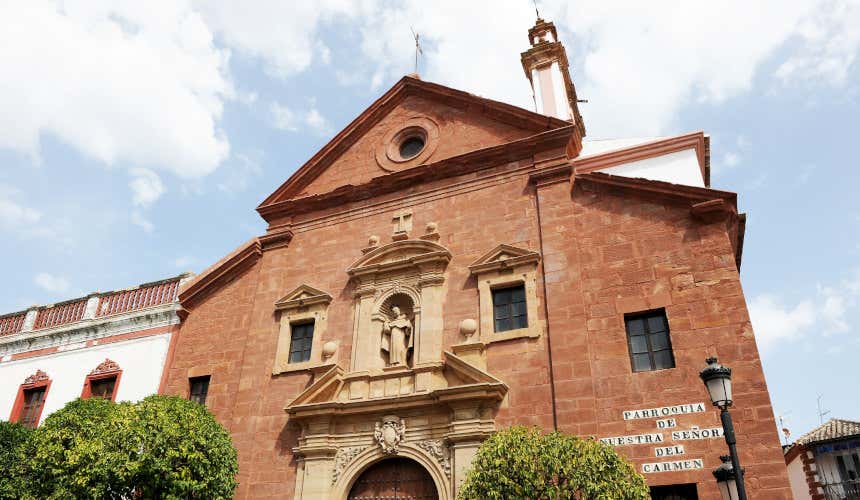 Parroquia de Nuestra Señora del Carmen, una iglesia de color rojizo y con una gran escultura en su pórtico 