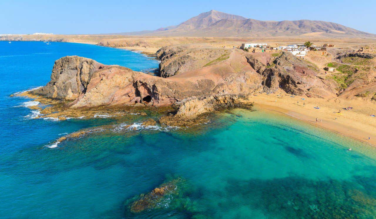 Montañas, arena dorada y aguas cristalinas en playa Papagayo, Lanzarote.