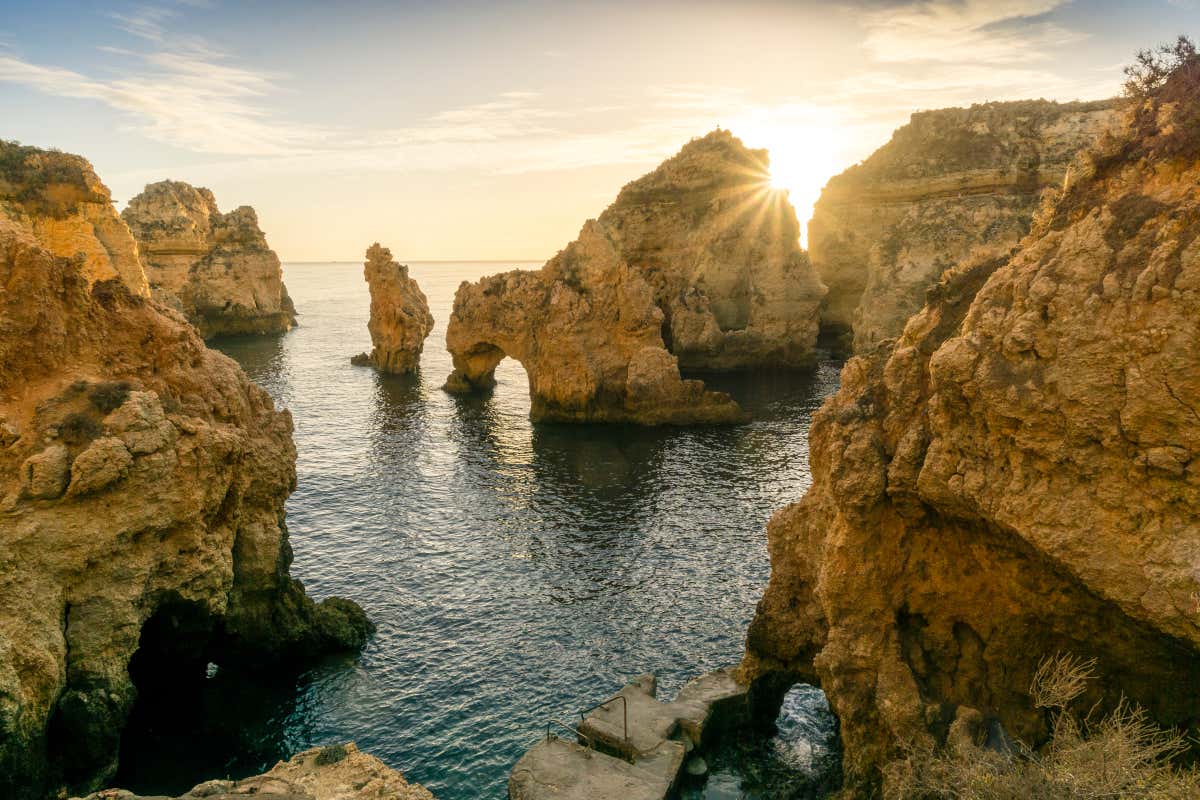 Various towering rock formations  rise up from the sea during a sunset, tranquil waters below going through the caves at one of the best beaches in Algarve