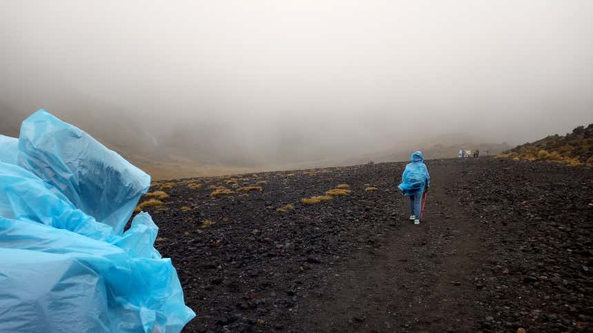 Alcuni escursionisti con indosso impermeabili monouso azzurri che percorrono i remoti paesaggi di Cropp River, il luogo più umido di tutta la Nuova Zelanda