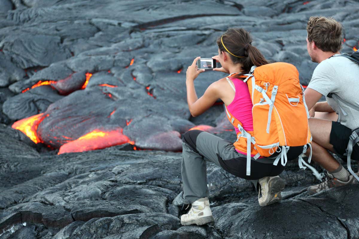 Deux touristes en tenue de sport, de dos, prennent des photos des coulées de lave de Kīlauea à Hawaï