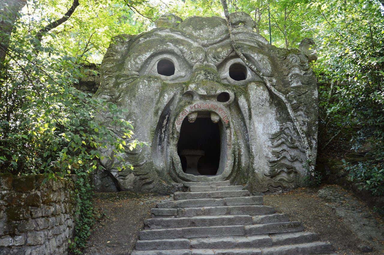 Una scultura di un mostro con la bocca spalancata nel giardino di Bomarzo