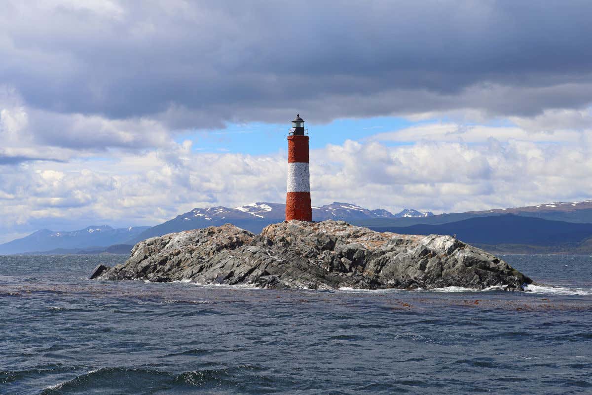 Phare rouge et blanc érigé sur des rochers et entouré par la mer, avec des montagnes en arrière-plan