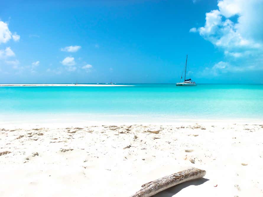 Catamarano sulle acque turchesi di Playa Mal Tiempo, con nuvole a destra e a sinistra, una sottile lingua di sabbia bianca sulla sinistra e un tronco in primo piano a destra