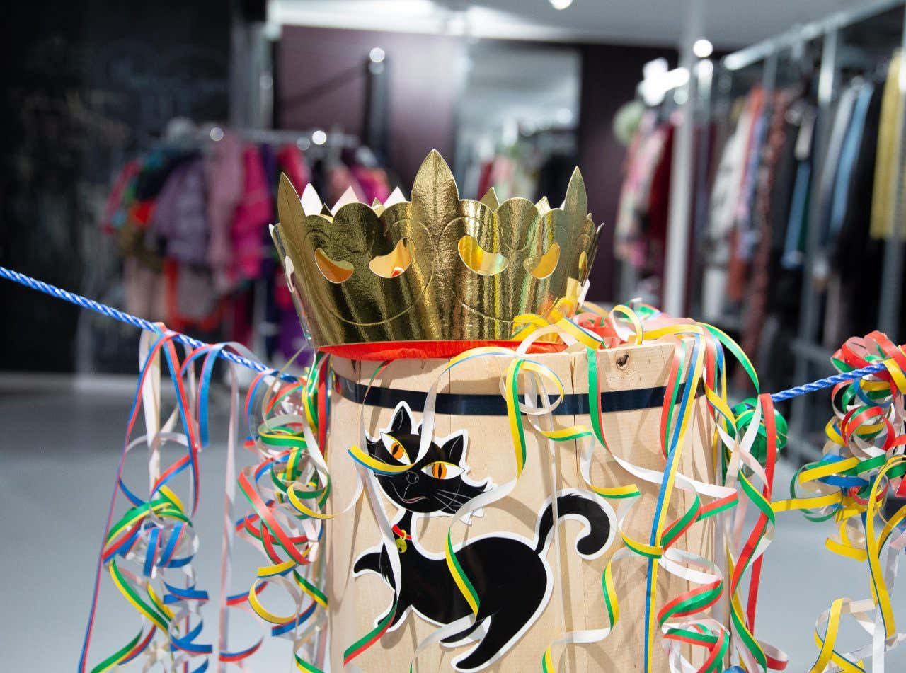 A paper cut out of black cat on a barrel with a gold crown on top, decorated with colorful ribbon hanging off the barrel