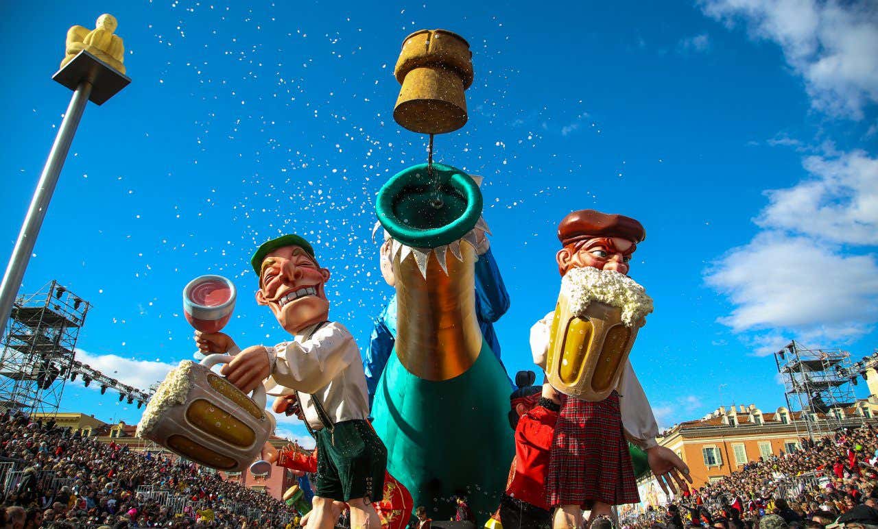 Image looking up at 3 effigies, two holding big beers and the one in the middle being a champagne bottle against a vibrant clear blue sky