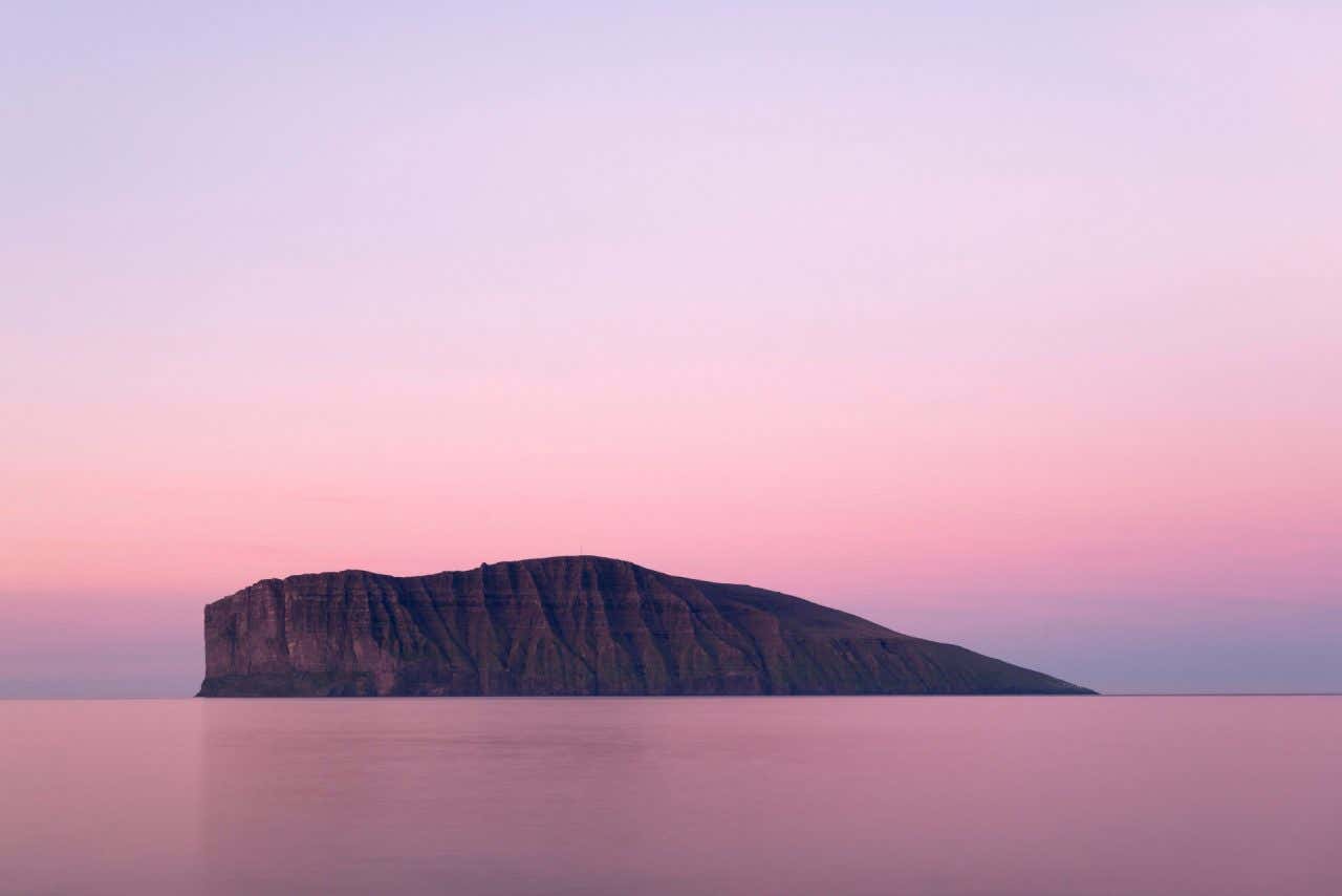 Panoramica dell'Isola di Fugloy che si staglia contro un cielo rosa il cui colore si riflette sul mare