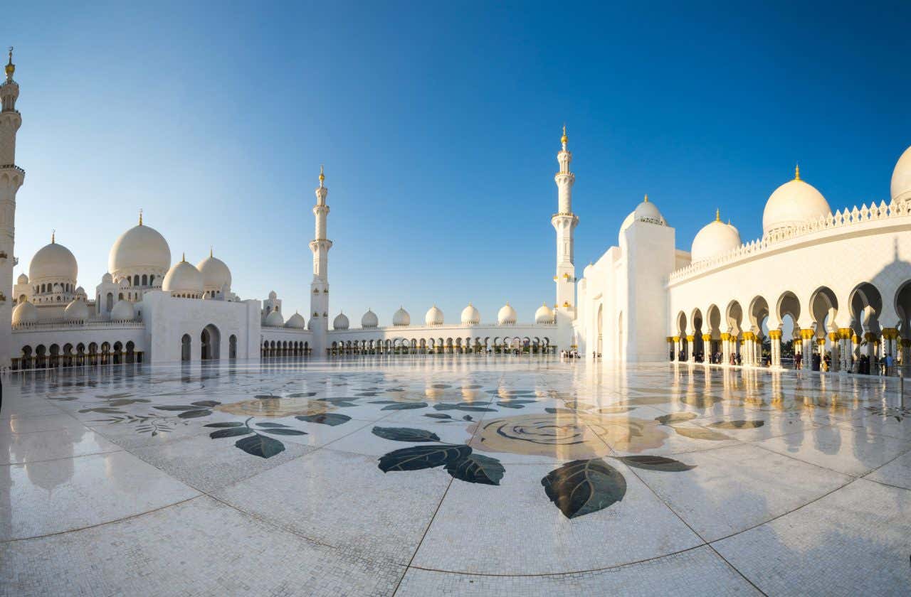 Cour intérieure au carrelage blanc décoré, avec ses arches, ses dômes et ses minarets en arrière plan