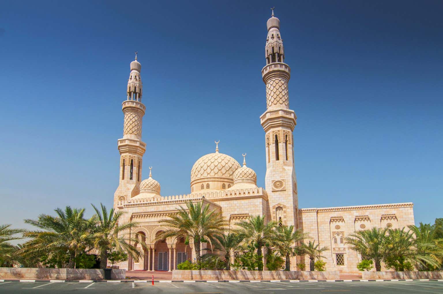 La moschea di Jumeirah, una delle attrazioni principali di Dubai, si erge contro il cielo azzurro e circondata da palme, con una costruzione a mattoni e sovrastata da cupole e due imponenti minareti.