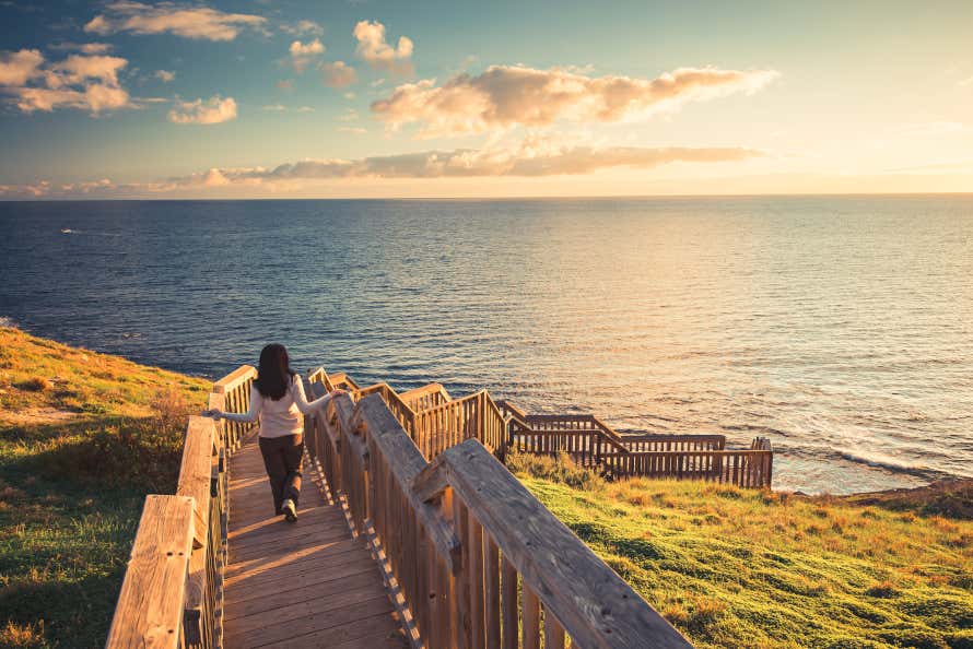 Uma mulher descendo uma passarela que leva ao mar ao pôr do sol