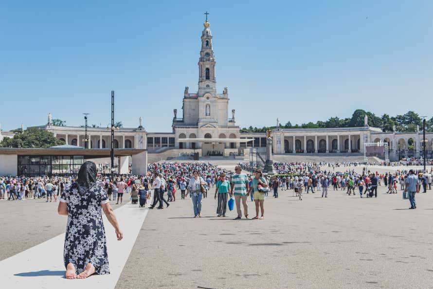 Mulher rezando no Santuário de Fátima, em Portugal com visitantes ao fundo