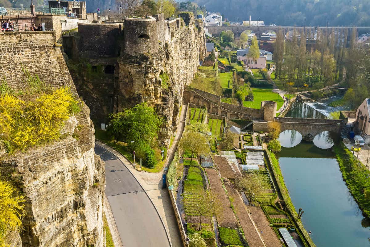 Tall fortifications with vegetation next to two stone bridges that cross the Alzette River on a sunny day