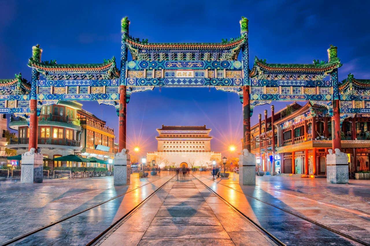 A grand blue and gold Chinese gate over a large square, under a dark blue sky and lit up at night