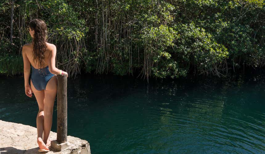 Uma mulher de costas contemplando as águas do cenote de Chucumaltik