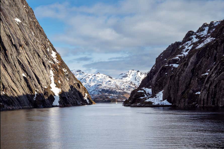 Trollfjord, a fjord in the Lofoten Islands, Norway. Steep cliffs meet the sea with snowy mountains in the background.