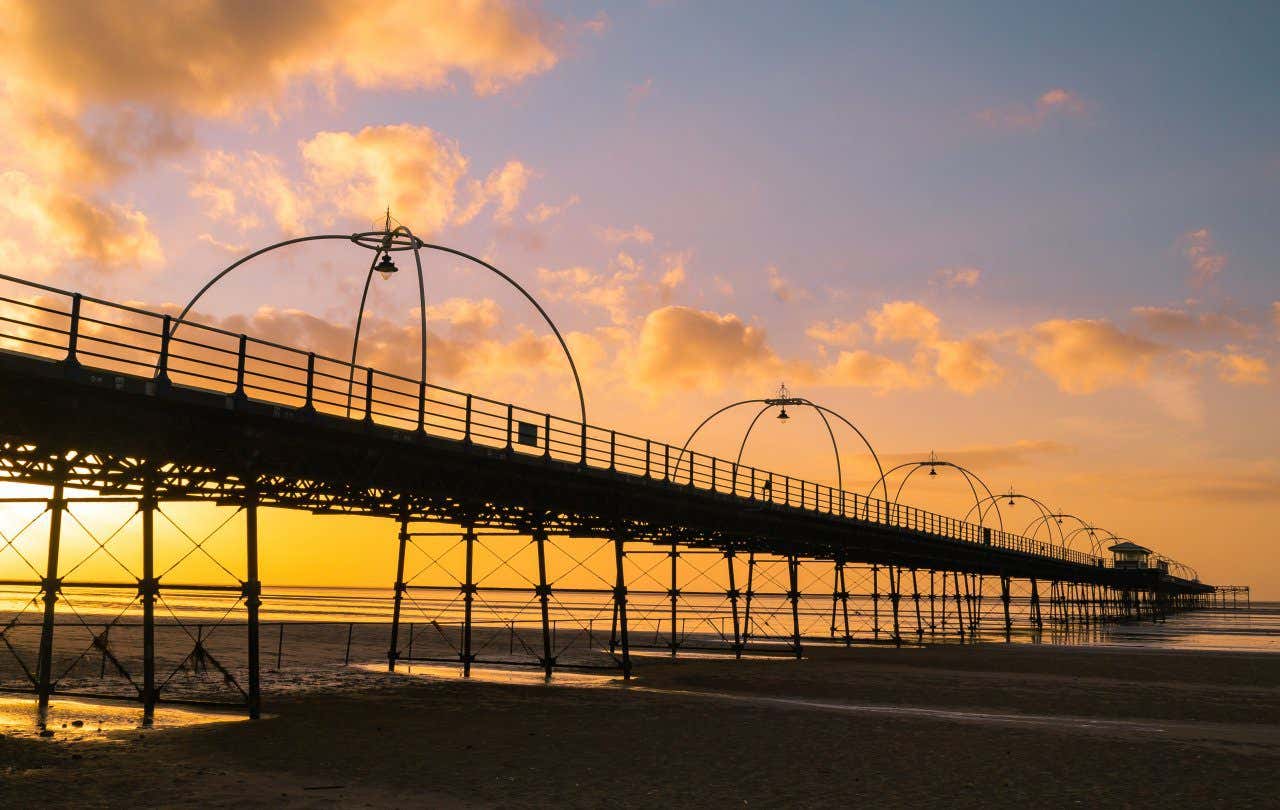 A long metal pier over a sandy beach and sea under a golden sky at sunset in Southampton