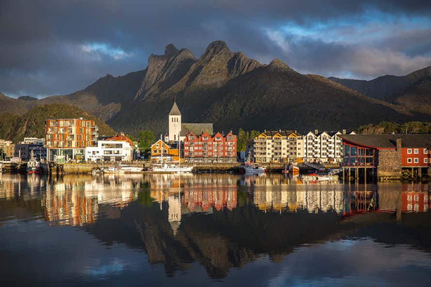 Svolvaer, the capital of the Lofoten Islands in Norway. Residential buildings and a church on the calm waterfront with mountains in the back.