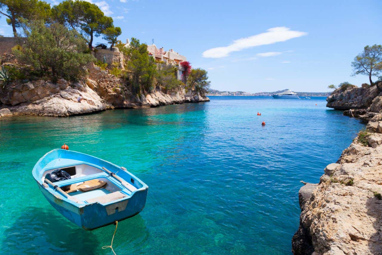 Barco azul nas águas cristalinas de Cala Fornells e um grande navio ao fundo