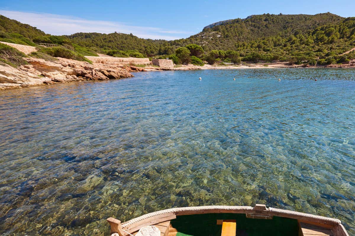 Aguas cristalinas entre las que se divisa el fondo marino en una de las calas de Cabrera, con un pequeño barco en primer plano.