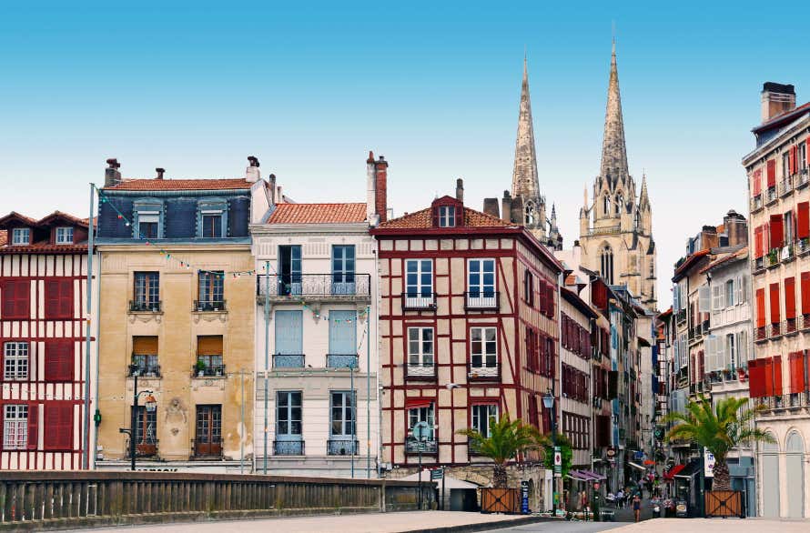 White and reddish four-storey buildings with coloured beams and shutters and a two-towered church, a mixture of French and Basque architecture.