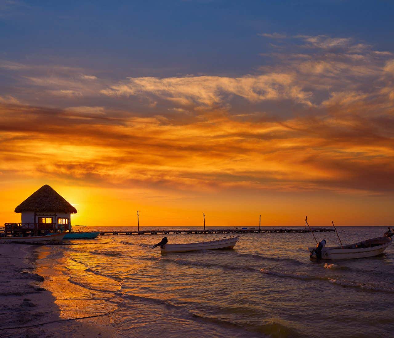 A sunset over a beach in Holbox with boats floating near the shore