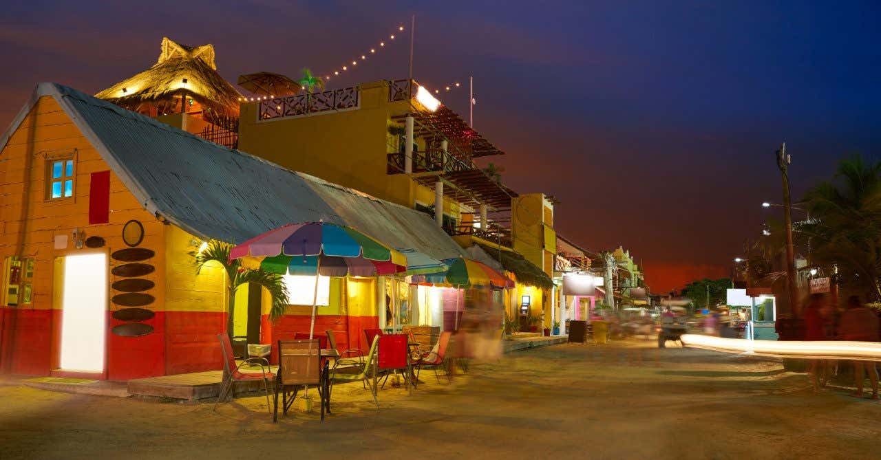 A yellow and red wooden hut with outdoor tables under colourful umbrellas at night time