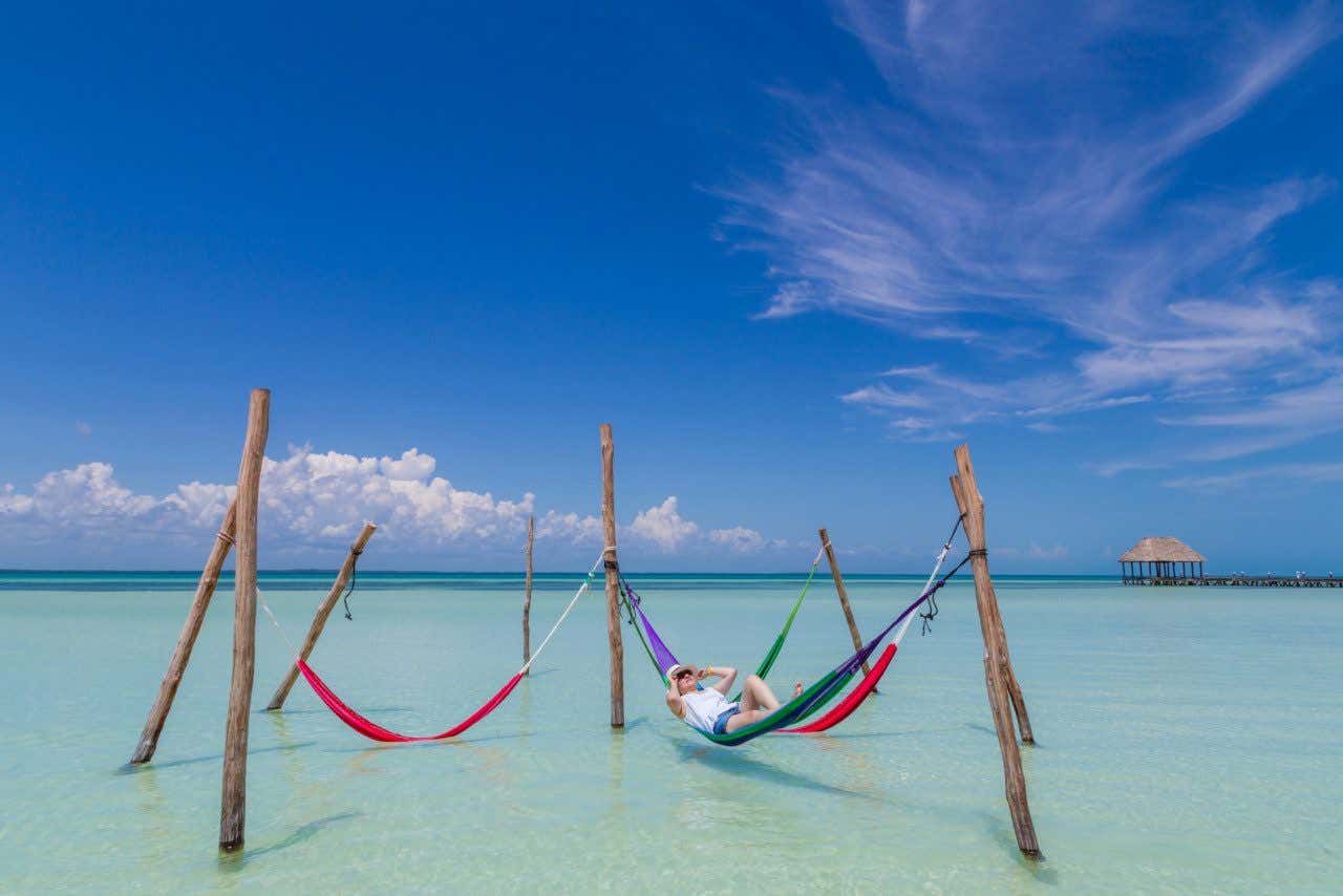 A man wearing a hat and sunglasses relaxing in a hammock on a paradisiacal beach in Holbox