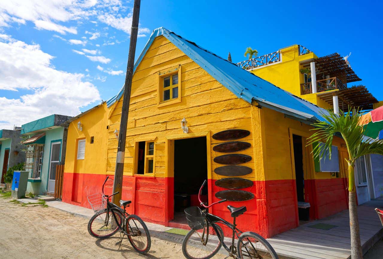 A yellow and red wooden hut with a blue roof and two bikes parked in front of it