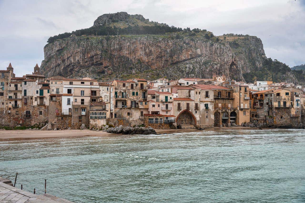 Scorcio di Cefalù, con delle case tipiche affacciate in riva al mare e un imponente promontorio di roccia a fare da sfondo