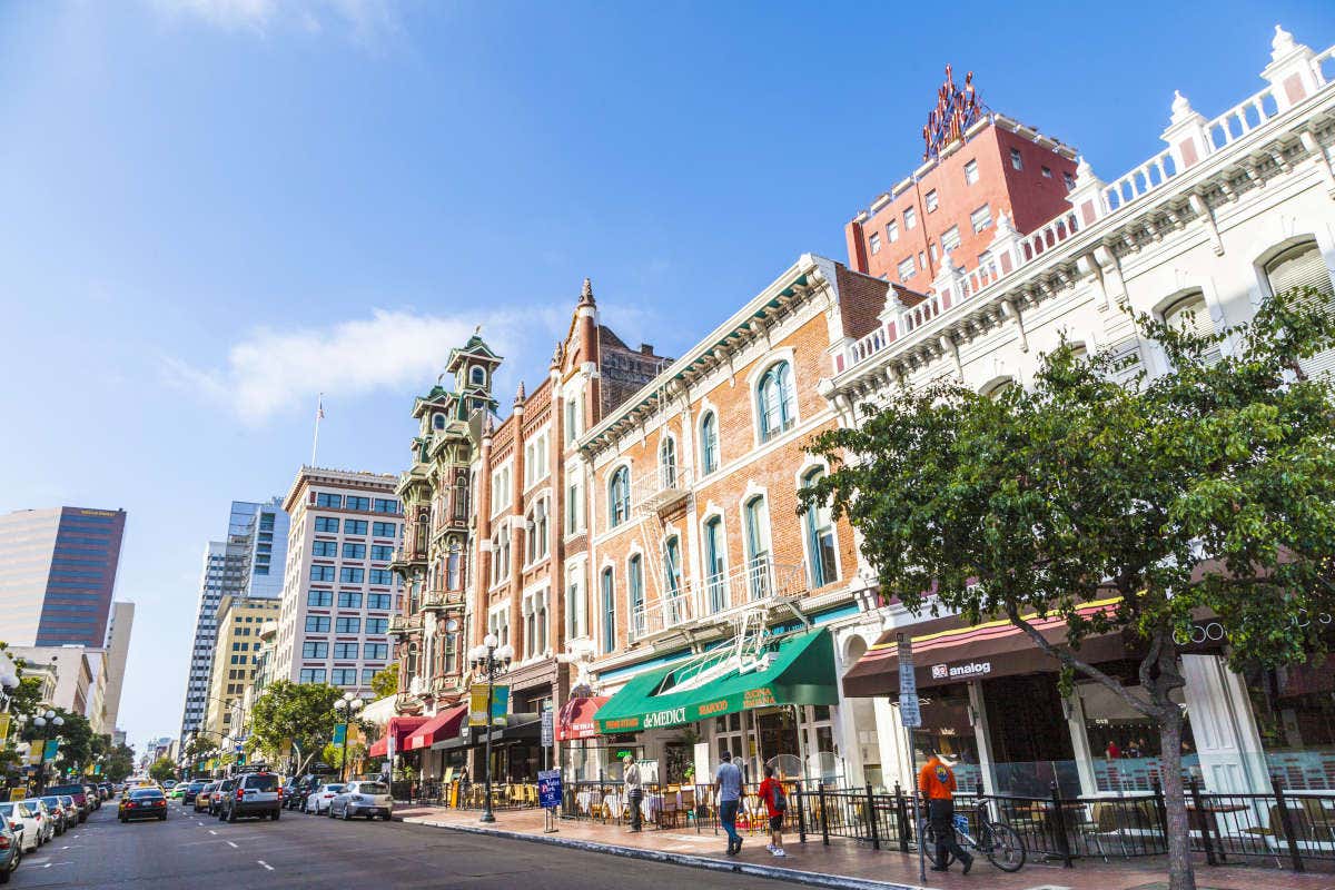 Facades of San Diego's Victorian houses on a sunny day along a busy street with cars and pedestrians