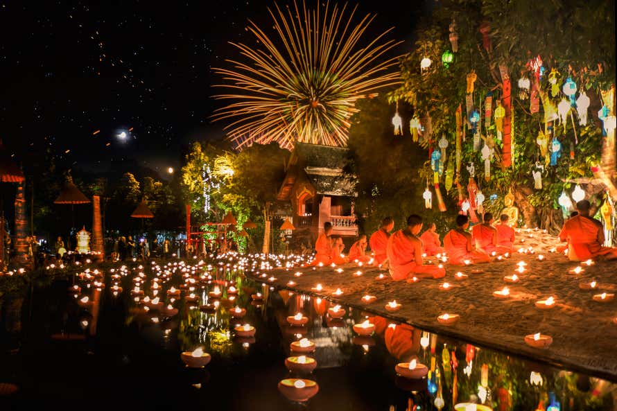 Monaci buddisti, luci e candele durante un festival di novembre in Thailandia, con fuochi d'artificio sullo sfondo