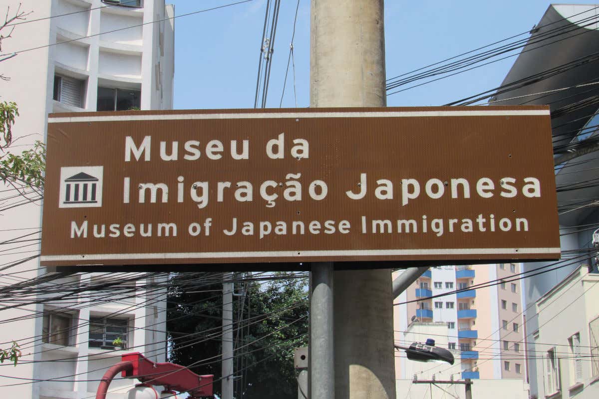 Uma placa em um poste cheio de cabos que indica a localização do Museu da Imigração Japonesa de São Paulo